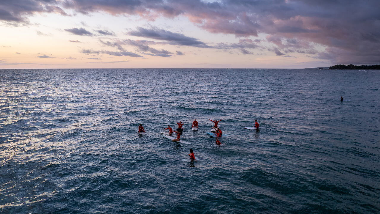 Surf & Service attendees float on surf boards in the ocean at sunset