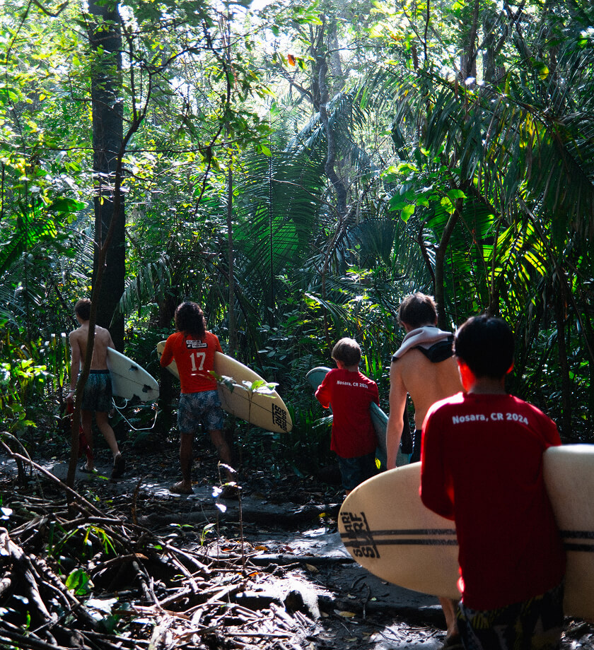 Surf & Service attendees walk with their surfboards through the jungle