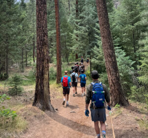 Group of teenagers hiking along a forest trail surrounded by trees and greenery.